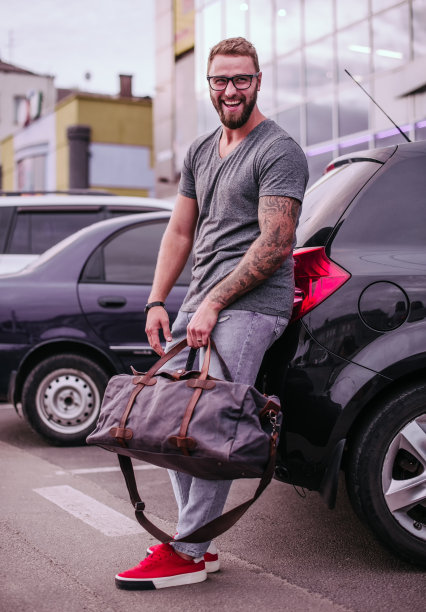 千禧一代男子身穿休闲服装，戴着眼镜，拿着旅行包图片下载