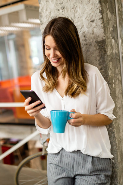 一个快乐的年轻成功女性的肖像使用智能手机和喝咖啡在休息图片下载