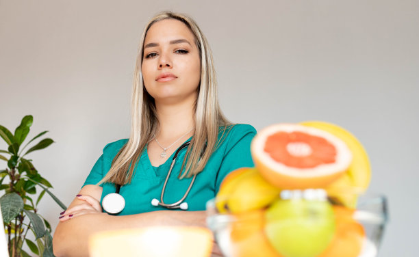 女性营养学家拿着水果在办公桌前工作。微笑的营养师在她的办公室，她正在展示健康的蔬菜和水果，保健和饮食的概念。图片下载