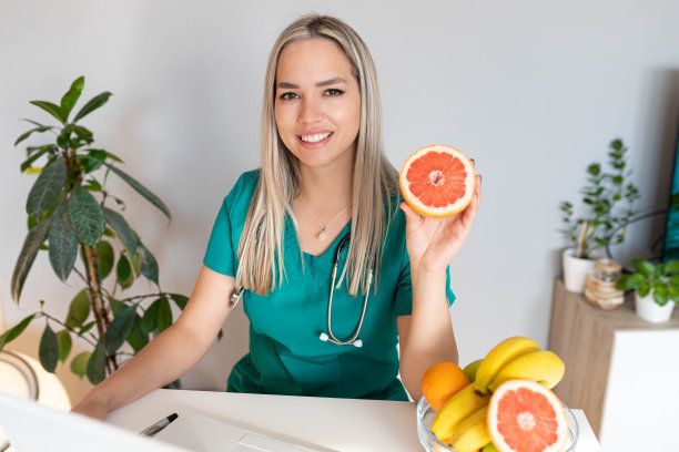 女性营养学家拿着水果在办公桌前工作。微笑的营养师在她的办公室，她正在展示健康的蔬菜和水果，保健和饮食的概念。图片下载