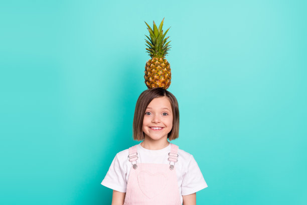 照片甜有趣的学校女生穿粉红色整体微笑抱着头菠萝孤立的蓝绿色背景图片下载