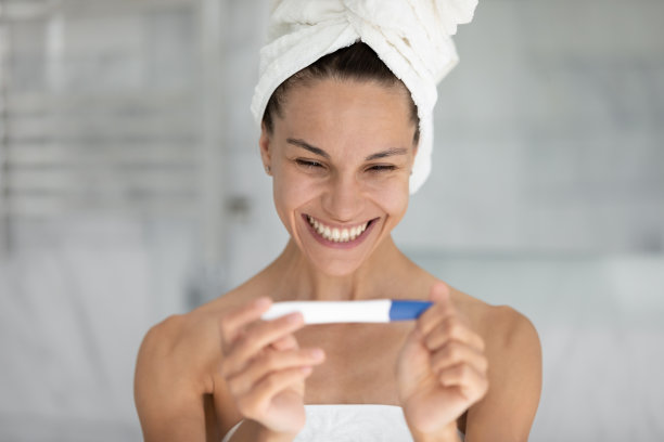 快乐美丽的年轻混血女人看着验孕棒。图片下载