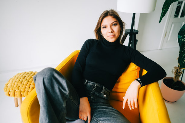 有吸引力的时髦白人年轻女子的肖像坐在客厅的扶手椅上，看着相机。图片下载
