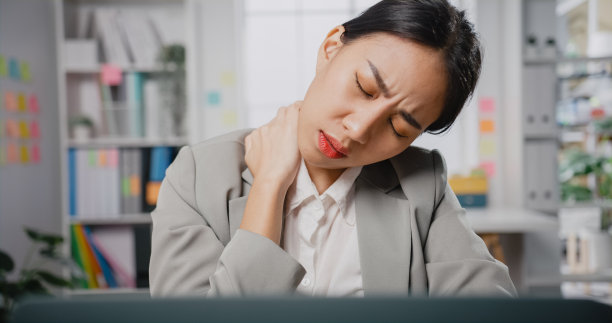 劳累过度的年轻亚洲女商人坐在办公桌上用笔记本电脑按摩僵硬的脖子，以缓解办公室肌肉的疼痛。图片下载