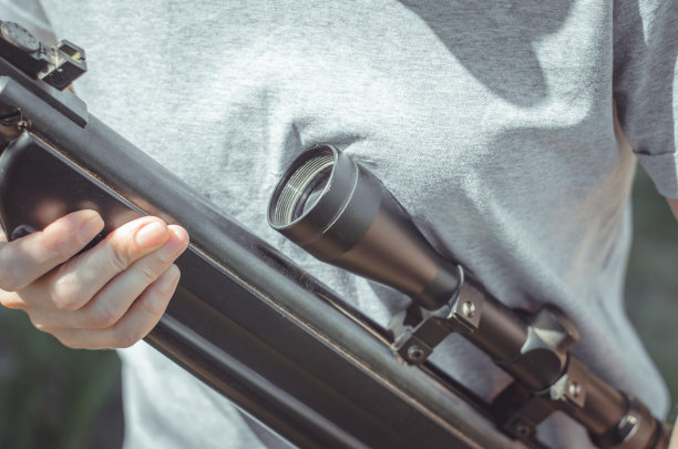 一个女人拿着一把大狙击步枪，特写。一个年轻女孩手里拿着枪。带光学瞄准具的气步枪图片下载