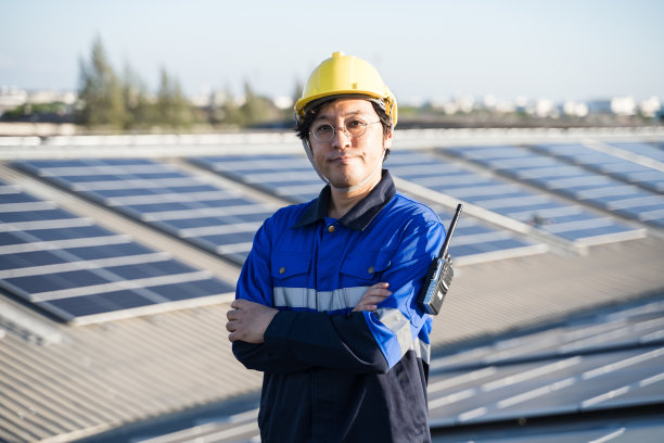 亚洲工程师的肖像在背景场的光伏太阳能电池板太阳能电池在屋顶的工厂。图片下载