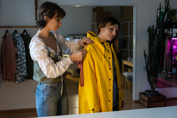 时装设计师工作室与女裁缝测量和试穿定制的黄色雨夹克。图片下载