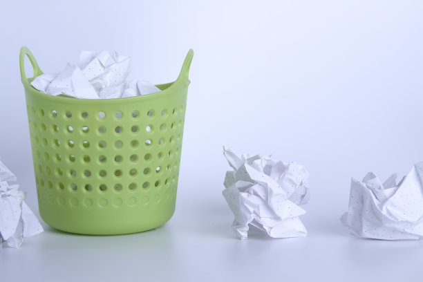 绿色的垃圾桶。完整的篮子里。放在篮子里的皱巴巴的纸。桌子上散落着堆积如山的垃圾。100%了。图片下载