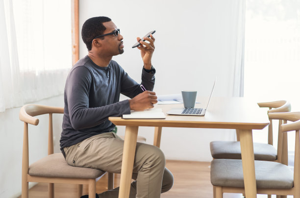 自信的自由作家非洲裔美国人在家里写笔记时激活智能手机上的虚拟数字语音助手。黑人让手机ai助手上网搜索信息。图片下载