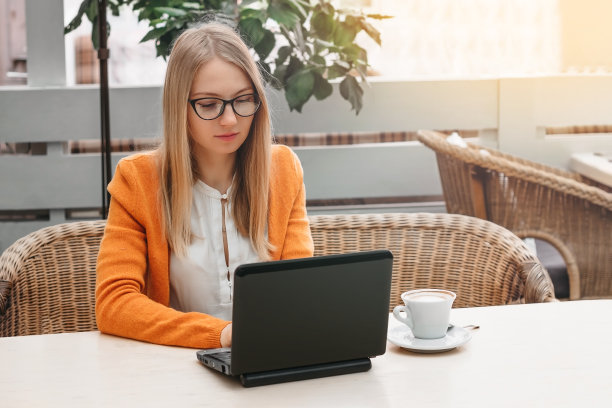 年轻的自由职业者，用笔记本电脑工作。咖啡厅里的金发女孩，手提电脑和一杯咖啡图片下载