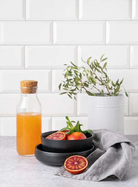 鲜榨橙汁装在瓶子里放在厨房的桌子上，盘子里放着新鲜的红橘子。健康饮料的概念。正面视图和拷贝空间图片下载