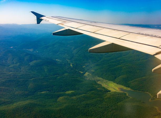 飞机机翼的观点，蓝色的天空和绿色的土地着陆。飞机窗口视图。图片下载