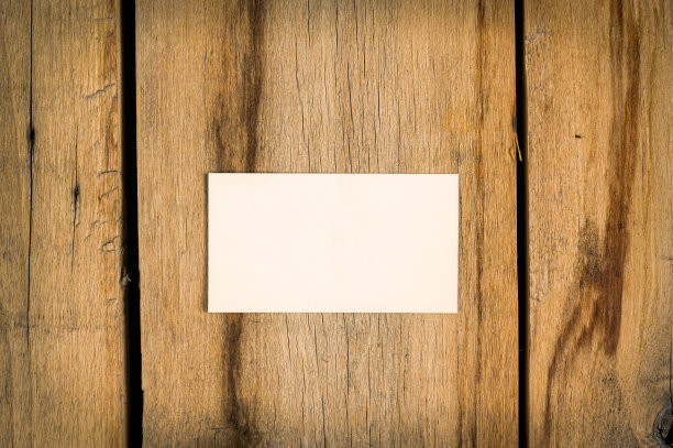 一张木制背景的空白名片。一个白色的长方形纸躺在有裂缝的旧木板上。有选择性的重点。图片下载