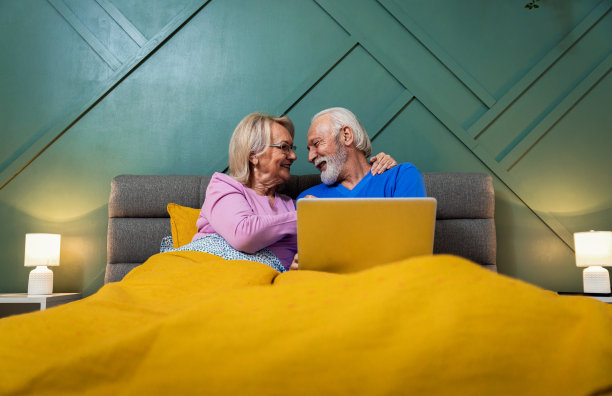 老年夫妇躺在卧室的床上使用笔记本电脑。图片下载