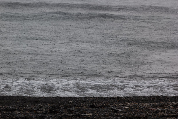 阴郁的大海在风暴与光滑的波浪与雨滴和黑色的火山海岸线，冲浪与泡沫，纹理，背景。图片下载