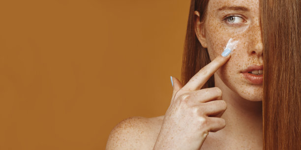 年轻漂亮的姜黄女子在脸上涂面霜图片下载