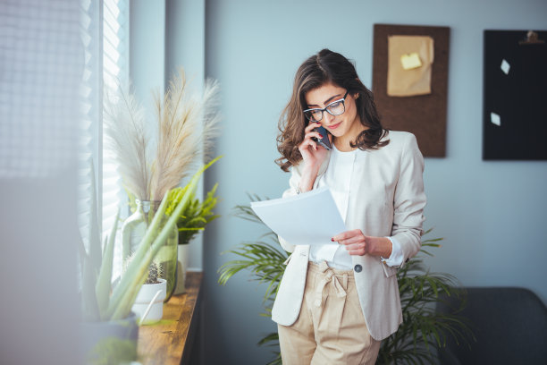 一位年轻的女商人站在酒店房间里使用手机。图片下载