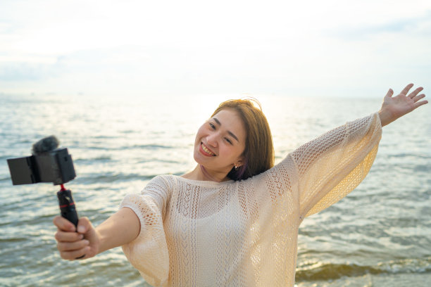 亚洲网红在海滩日落时录制短视频。图片下载