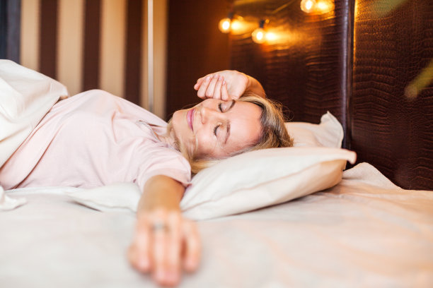 快乐的中年妇女坐在床上伸展手臂图片下载