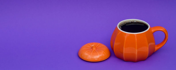 橙色的咖啡杯，南瓜形状，时髦的紫色背景。万圣节节日早晨的概念。图片下载