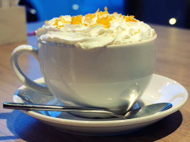 桌上放着一杯卡布奇诺，上面撒着鲜奶油和橘子皮。特写照片图片下载