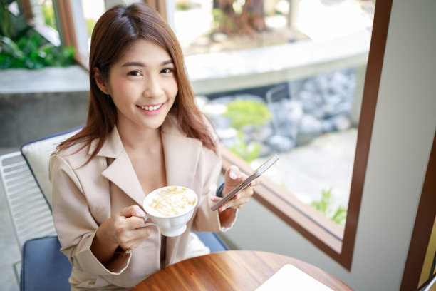 迷人的亚洲女商人在工作期间使用智能手机的笔记本电脑图片下载