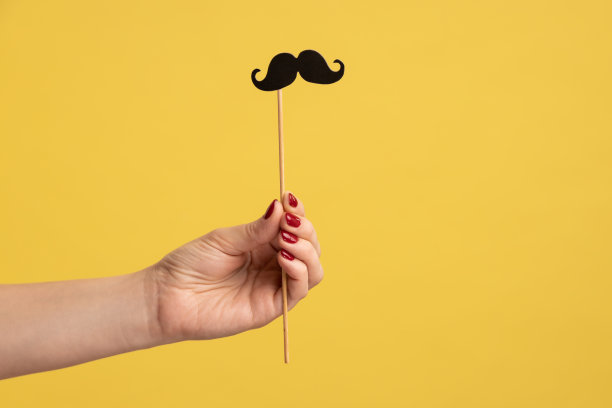 特写侧视图的女人手握节日派对道具，黑色小纸胡子粘上。图片下载