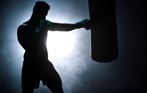 在黑暗健身房里与沙袋搏击的拳击男人剪影。男性运动员为即将到来的比赛做准备。年轻武术家训练图片下载