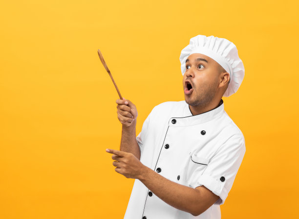 年轻英俊的亚洲男子厨师制服与帽子拿着勺子器皿烹饪在厨房的各种手势指向孤立的黄色背景。印度男子职业厨师餐厅和酒店图片下载