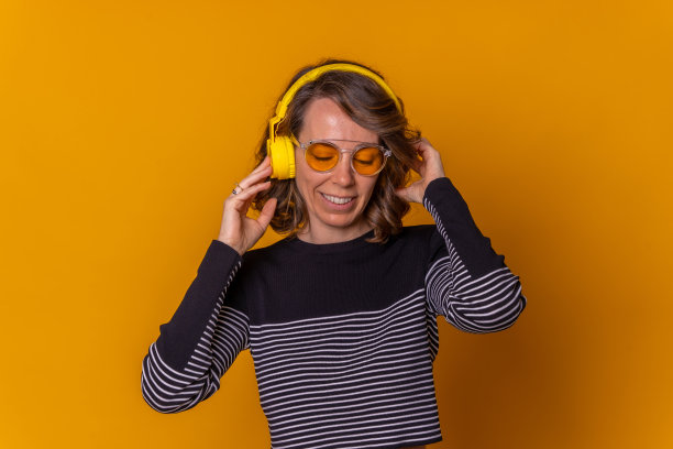 白人女孩听音乐微笑和跳舞与她的手机，耳机和墨镜，黄色的背景图片下载