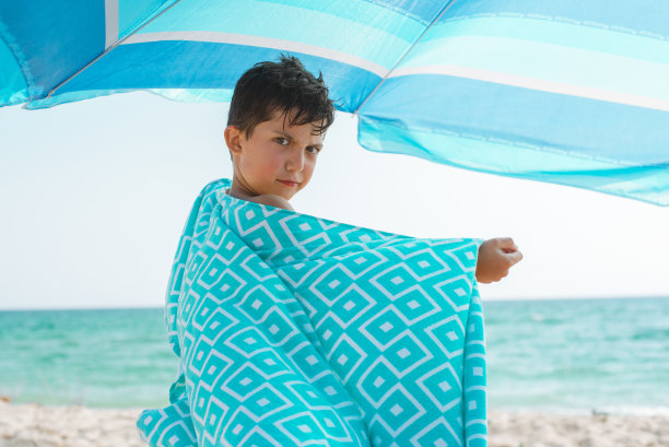 一个欢快的孩子裹着一条鲜艳的沙滩浴巾在沙滩上。图片下载