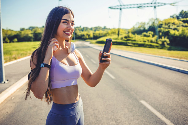 一个运动的年轻女子在户外运动时使用手机的照片。一个女人用她的智能手机发短信。女性跑步者在路上用手机发短信。图片下载