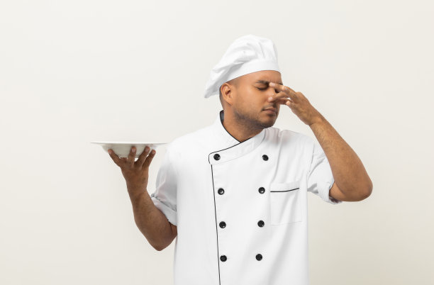 气味难闻，食物不好吃。年轻的亚洲厨师长捧菜有烂菜的味道和恶心。在单独的背景下和厨师一起弄脏食物。图片下载