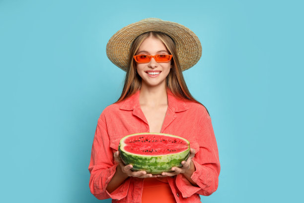 美丽的女孩与一半的西瓜在浅蓝色的背景图片下载