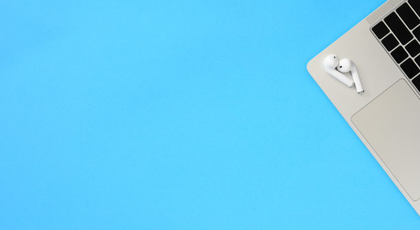 白色无线耳机放在笔记本电脑边缘，蓝色背景。图片下载