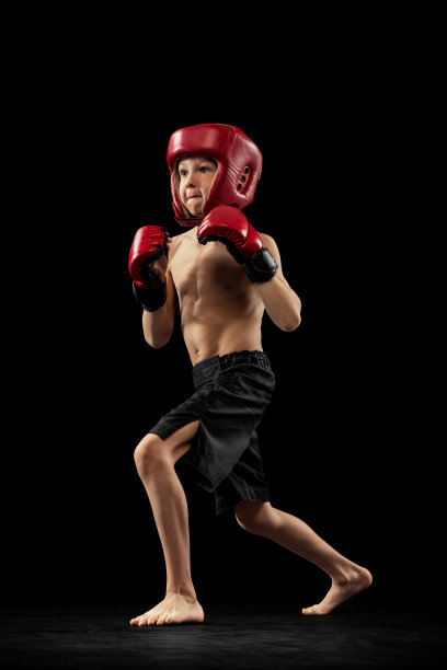 摄影棚拍摄的学龄前男孩，可爱的孩子在运动镜头和手套训练单独在黑色背景。运动，教育，动作，运动概念。图片下载