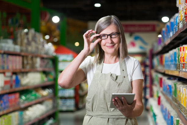 杂货店高级女售货员的肖像，头发花白的女人带着平板电脑微笑着看着相机图片下载