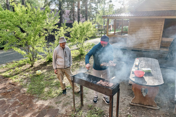 一位亚洲老人和他已成年的儿子在后院的烧烤架上烧肉。图片下载