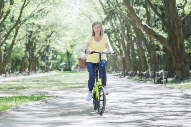 积极的生活方式。高级美丽运动的女人骑着黄色的自行车在公园，户外。他走了，看着镜头，微笑着图片下载