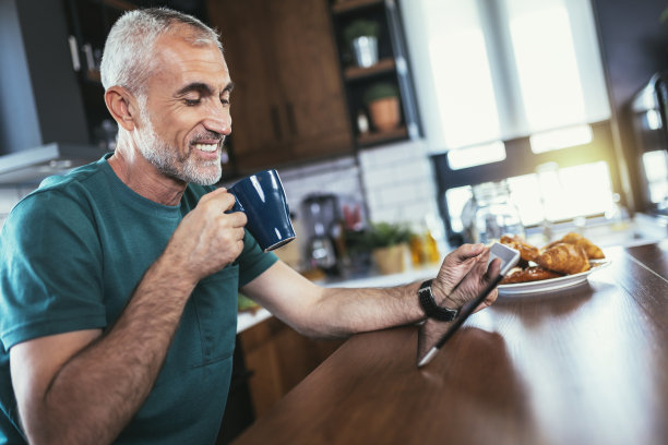 成熟的厨房男人在家使用数字平板电脑工作图片下载