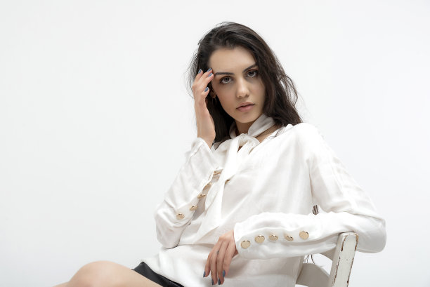 年轻美丽的照片模特穿着薄织物，夏天的白衬衫和白裤子，在白色背景的工作室里摆出艺术的姿势。图片下载