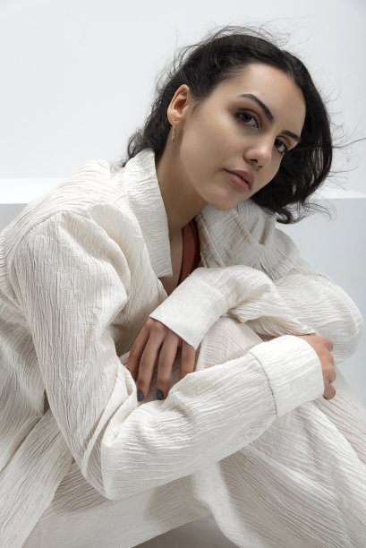 年轻美丽的照片模特穿着薄织物，夏天的白衬衫和白裤子，在白色背景的工作室里摆出艺术的姿势。图片下载