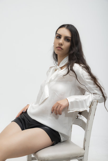 年轻美丽的照片模特穿着薄织物，夏天的白衬衫和白裤子，在白色背景的工作室里摆出艺术的姿势。图片下载