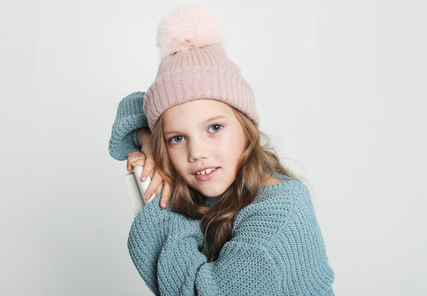 快乐的小女孩穿着蓝色毛衣和白色背景的冬季帽子图片下载