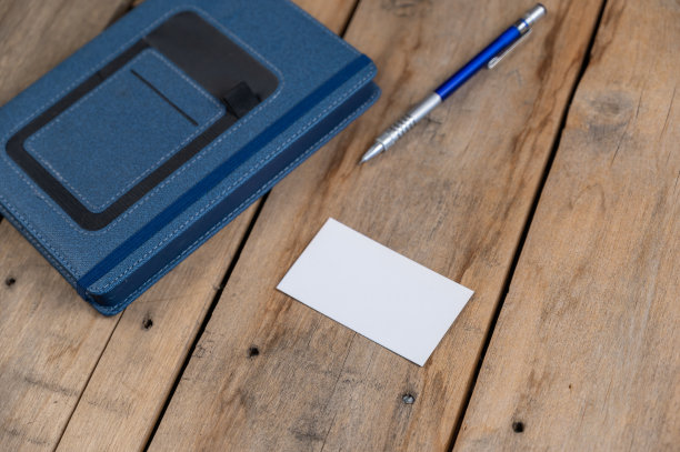 蓝色日记，名片和铅笔对面的木制背景。精装笔记本关闭。白色空白名片。银蓝色的金属铅笔放在有裂缝的旧木板上。有选择性的重点图片下载