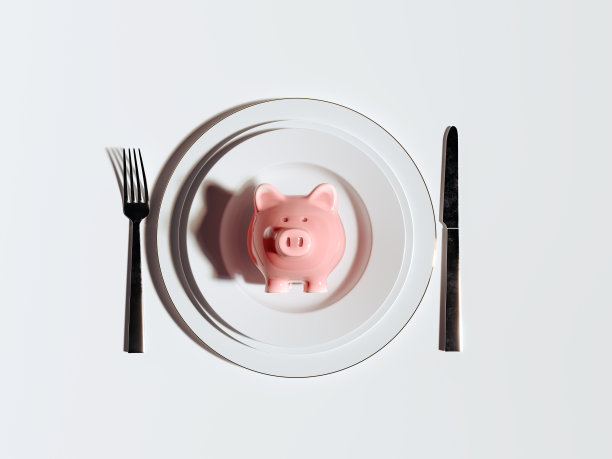 猪储蓄罐装在白色盘子里，配有刀叉。储蓄危机概念背景图片下载