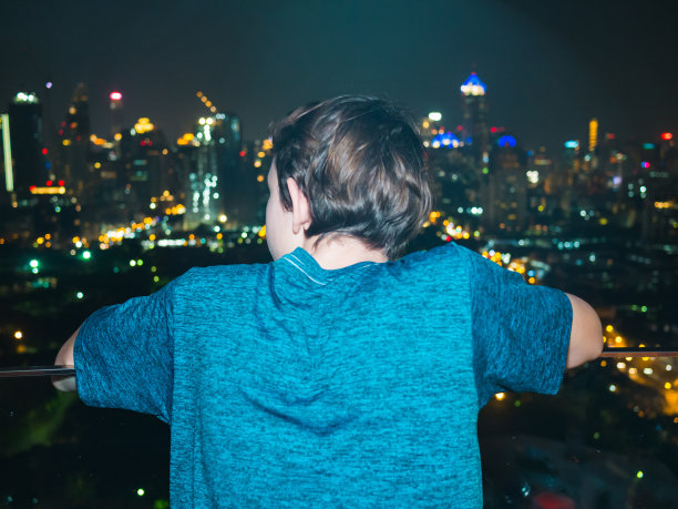 一个十几岁的男孩的后视图，他正在看曼谷的天际线，泰国图片下载