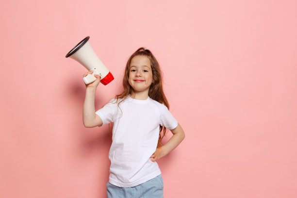 开朗可爱的小女孩，穿着白色t恤的孩子拿着扩音器隔离在粉红色的背景上。儿童情感概念、时尚、美容、学校和广告概念图片下载