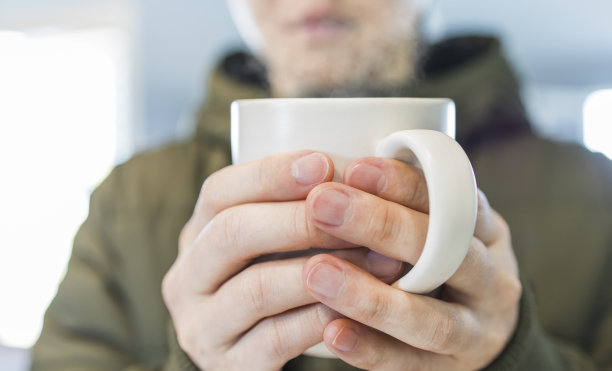 在寒冷的天气里捧着热水杯的男人。图片下载