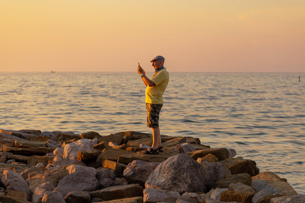 一位老人用手机拍下了大海和日落的照片图片下载